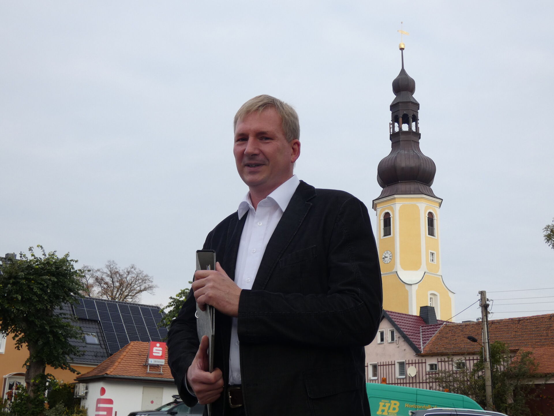 Bürgermeister Herr Meltke steht vor der Kirch in Hochkirch und lächelt in die Kamera