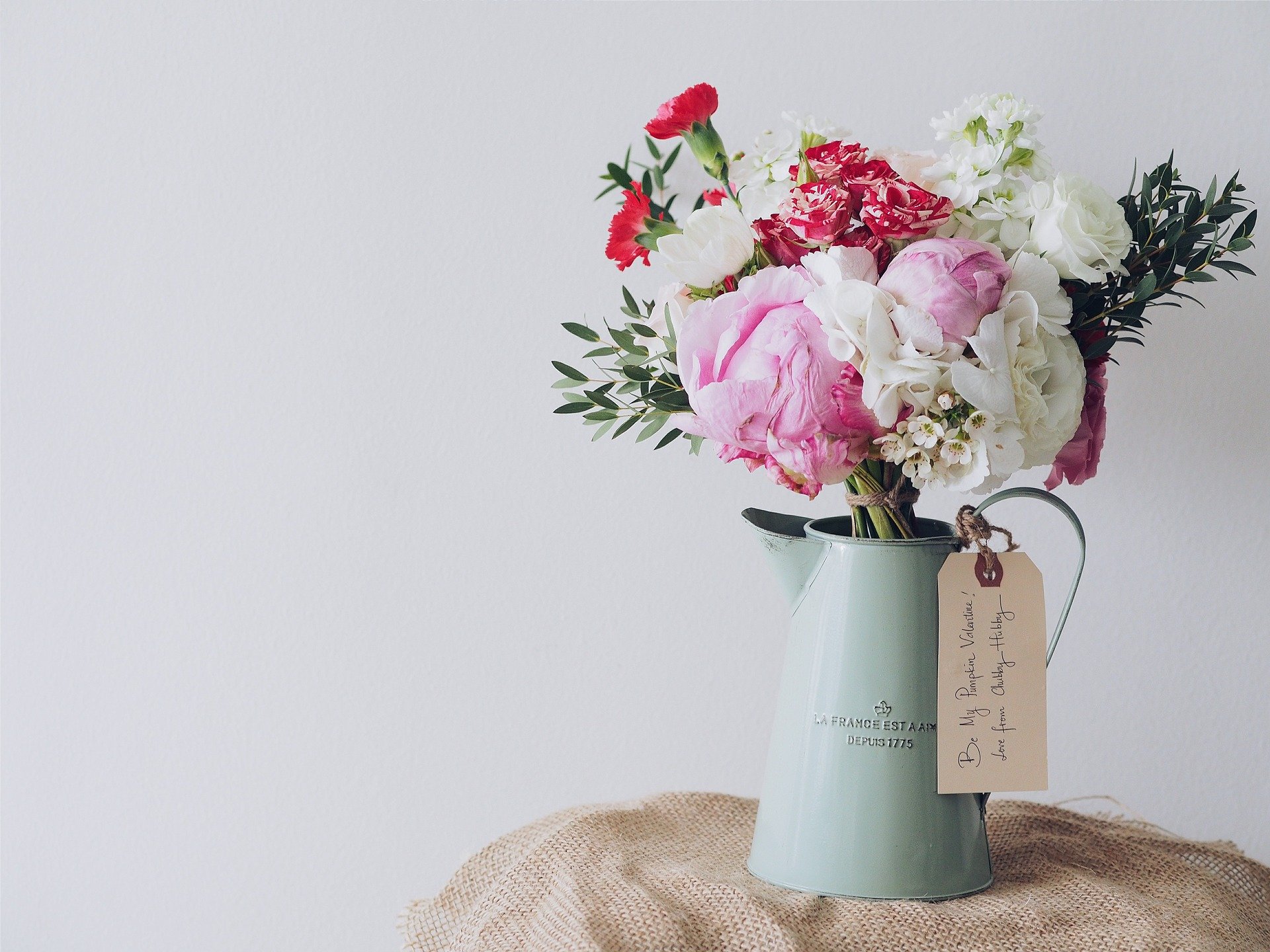 Ein bunter Blumenstrauß mit Pfingstrosen und roten Nelken in einer Vintage-Kanne, symbolisiert Wertschätzung der Gemeinde Hochkirch.